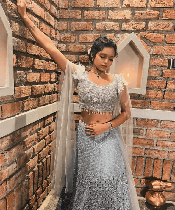 Neha Gupta wearing a stylish silver lehenga while posing indoors against a brick wall